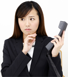 片手に受話器を持ち「苦手な電話対応は慣れるしかない」と思い込み困って悩んでいる女性イメージ
